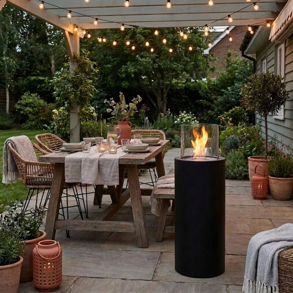 ScandiFlames Dualis Black bioethanol fireplace with lit flame on an evening patio, string lights overhead